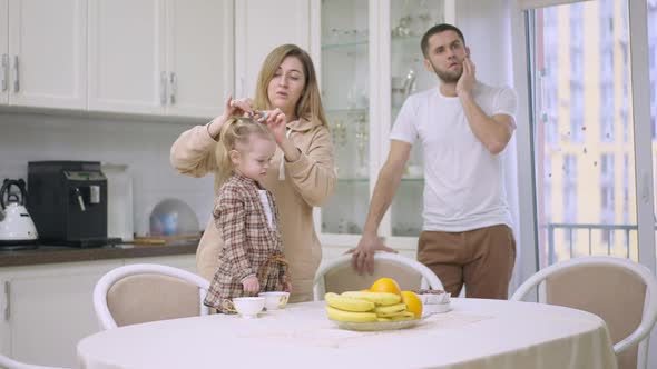 Woman Making Ponytails for Cute Little Baby Girl with Blurred Man Thinking Standing at Background As