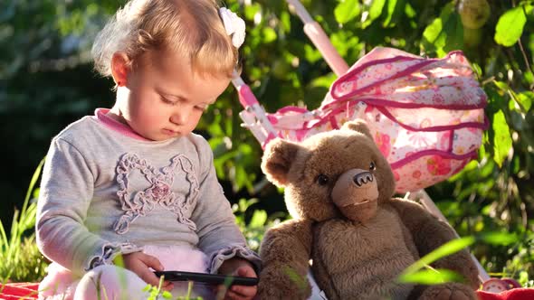 Little Girl Looks at Her Phone She is Sitting on a Blanket in the Garden