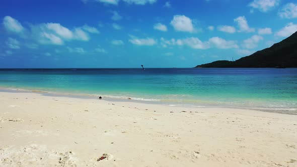 Paradise white sandy beach washed by waves of blue turquoise sea under bright sky with white clouds