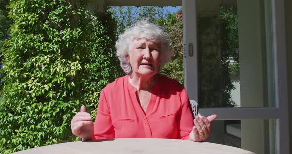 Caucasian senior woman sitting at table in sunny garden talking and gesturing