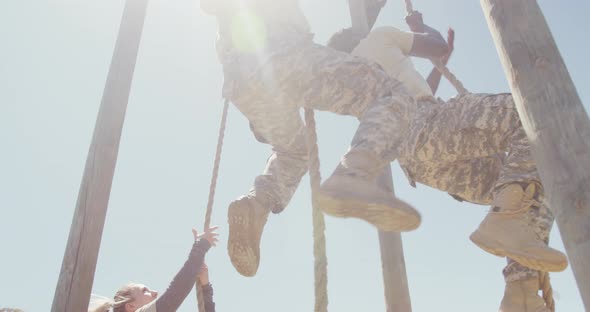 Three diverse fit male and female soldiers climbing ropes on army obstacle course