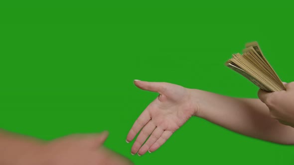 A male hand holds out a large bundle of money to a female hand, transaction, handshake, green screen