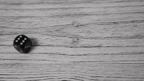 Black dice rolls and spins on a white textured wooden old table.