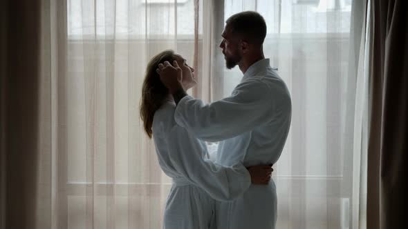 a Couple in White Coats Hugged and Stand at a Large Window