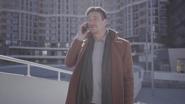 Portrait of Handsome Confident Man in Brown Coat Standing in the City Street Talking By Cell Phone