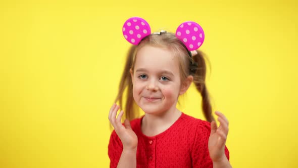 Joyful Beautiful Little Girl with Glowing Toy Mouse Ears on Head Dancing at Yellow Background