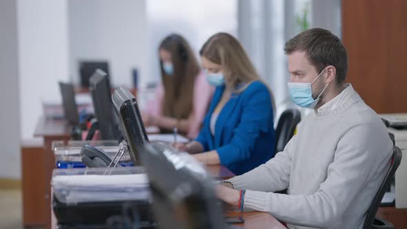 Rack Focus Along Concentrated Office Workers in Covid Face Masks Working Indoors