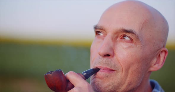 Contented Bald Farmer Smoking His Pipe On Field