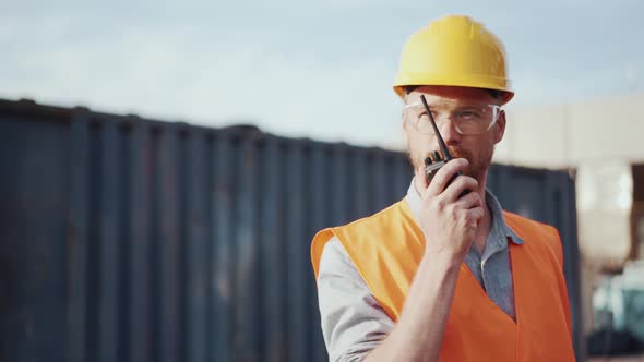 Confident man shipbuilder in helmet talking into walkie-talkie