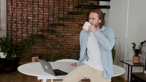 Man Drinks Coffee at the Workplace and Looks at the Camera