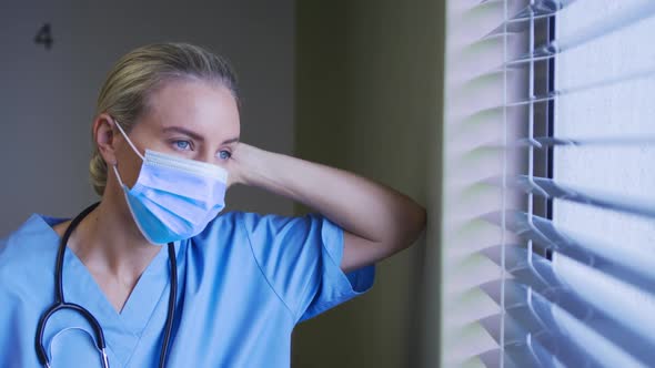 Portrait of caucasian female doctor wearing face mask looking through the window in hospital room