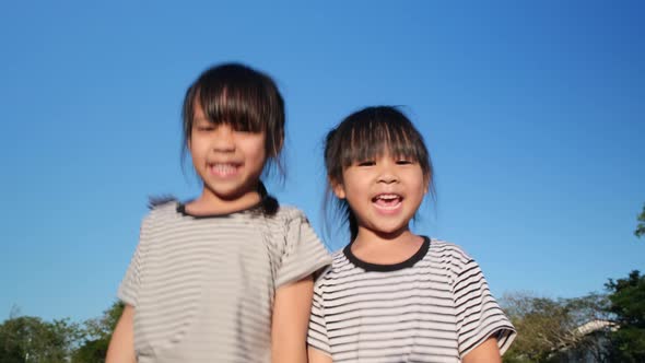 Happy Asian siblings girls hugging each other in the summer garden on a bright sky background.