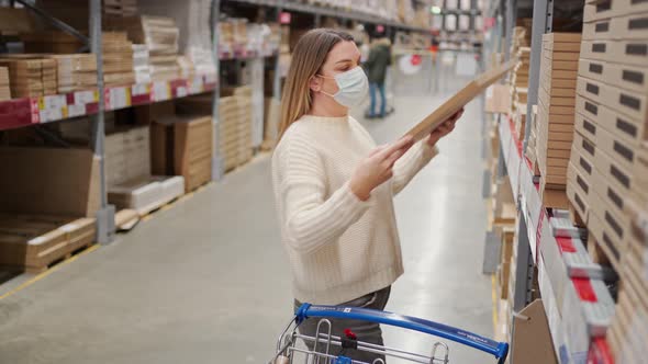 a Woman in a Protective Mask Takes Boxes in a Selfservice Warehouse in a Furniture Store
