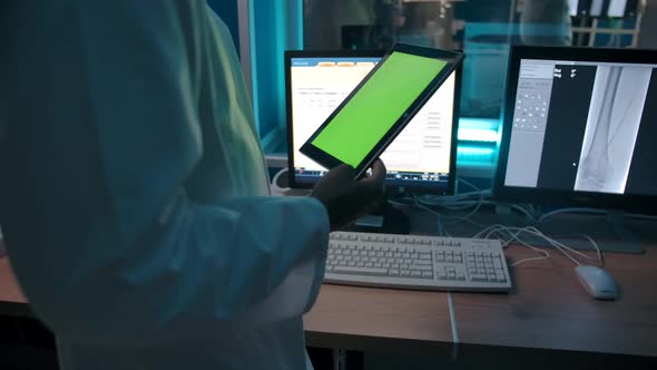 Doctor with a Tablet with a Green Screen Watching the Operation From the Control Room