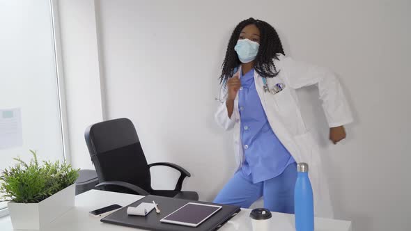 Black female doctor in medical mask dancing in clinic