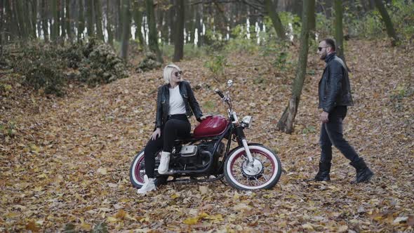 Happy Man in Sunglasses Comes to His Girl Sitting on Motorbike in Park