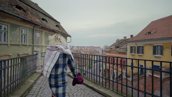 Woman reaching the top point of the old city with paint peeled walls buildings.