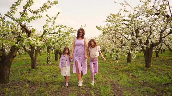 Mom Runs with Her Two Daughters in the Garden Among the Flowering Trees