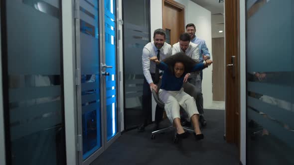 Multiethnic Colleagues Have Fun Ride Office Chair in Corporate Building Hallway