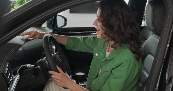 Young Beautiful Girl Chooses New Car at Car Dealership. The Woman Is Happy, Smiling and Rejoicing in