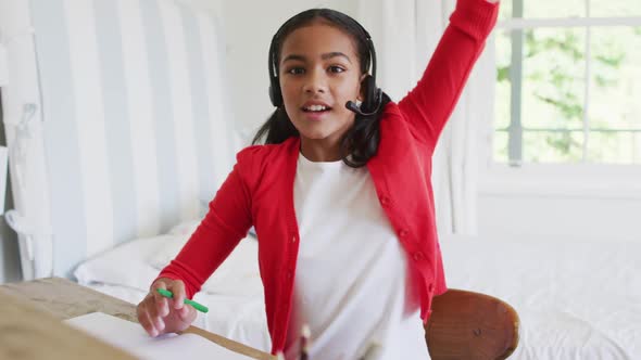 Mixed race girl at home in online school class, using headset raising hand