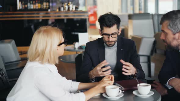 Bearded Businessman Speaking with Male and Female Partners in Modern Cafe