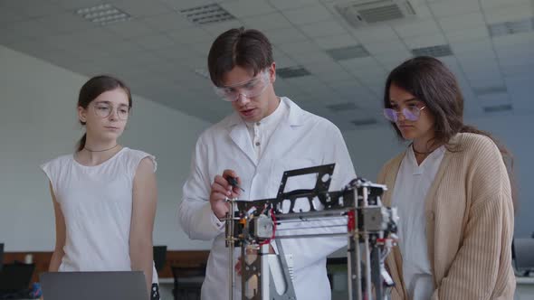 Teacher and Students Stand Above the 3D Printed Machine