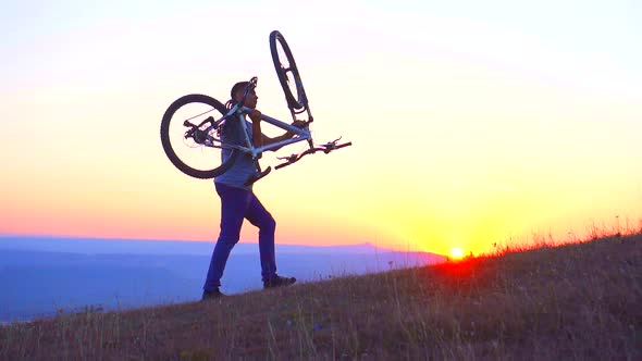 Man Carries a Bicycle of the Mountain at Sunsetslow Mo