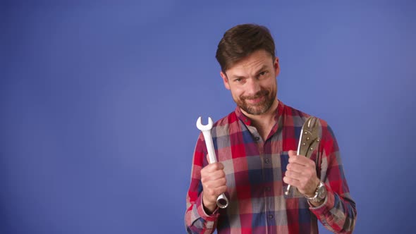 Young Bearded Unconfident Man Holding Tools and Smiles . Isolated