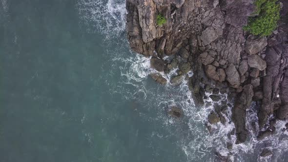 A birds eye view of a coast line with waves crashing on rocks.