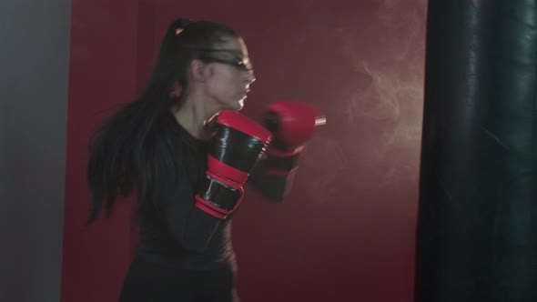 Young strong brunette woman vigorously punches and kicks a punching bag.