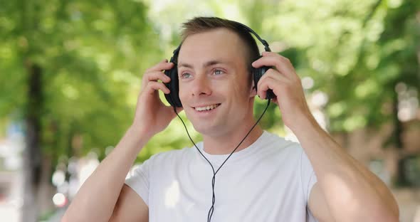 Smiling Man Puts on Big Headphones in the Summer City