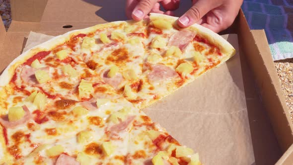 Hands Take Slices of Pizza From a Box on the Beach