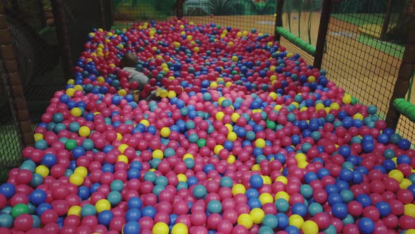 Child playing in pool with plastic balls on indoor playground in activity center.