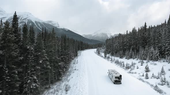 Aerial footage of a lonely trailer driving on a winter road through the forest in Alberta, Canada