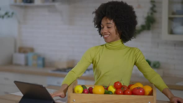 Joyful African American Housewife Searching Online Recipe on Tablet Standing in Kitchen with Raw