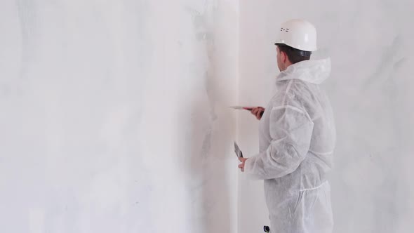A Man in a Protective Suit and Hard Hat Aligns the Walls in the House with Putty