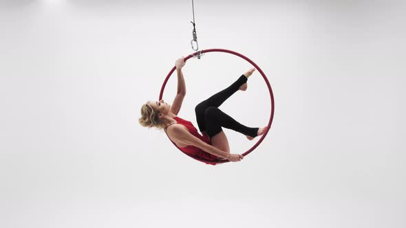 A Girl In A Red Dress Sits On A Hoop In Longitudinal Twine And Spins. White Cyclorama Location. 