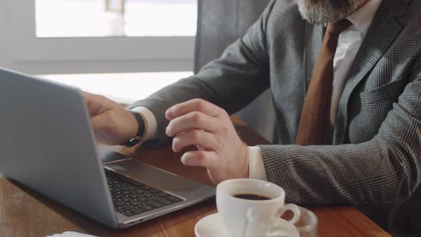 Senior Businessman Typing on Laptop at Cafe Table