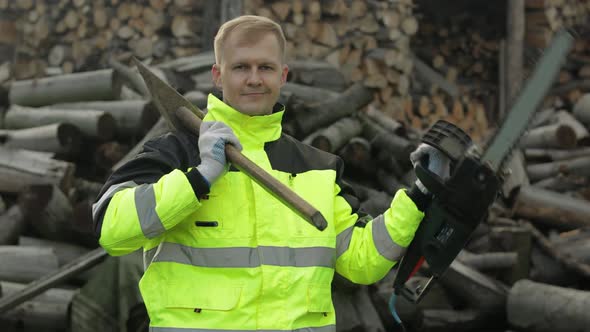 Lumberjack Worker. Man Woodcutter Holds Big Axe and Electric Chainsaw on His Hands. Firewood