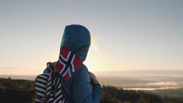 A Tourist with a Norwegian Flag in a Backpack Walks Through the Picturesque Highlands at Dawn