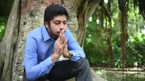 A depressed and heart broken Asian businessman is upset and feeling lonely and sitting under a tree