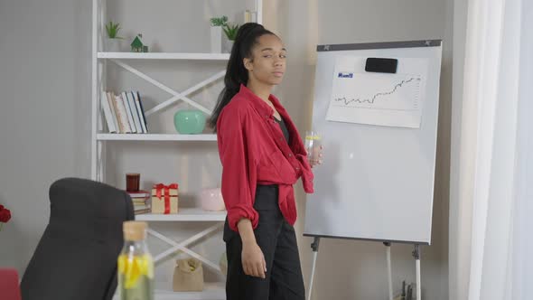 Side View of Slim African American Young Businesswoman Standing in Home Office at Business Graph on