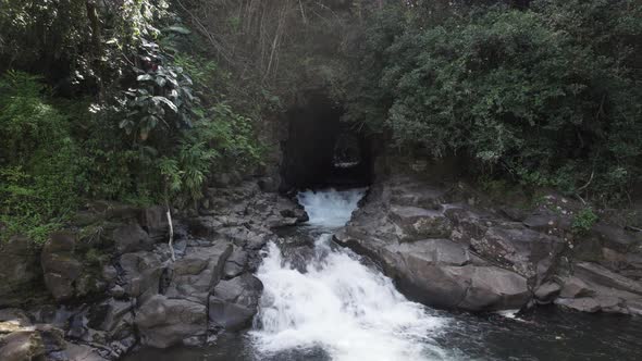 Low Aerial view showing flowing water out of natural lava tube into natural river pool in jungle of