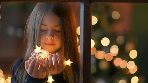 Happy cute girl holding bright festive garlands in her hands and dreaming.