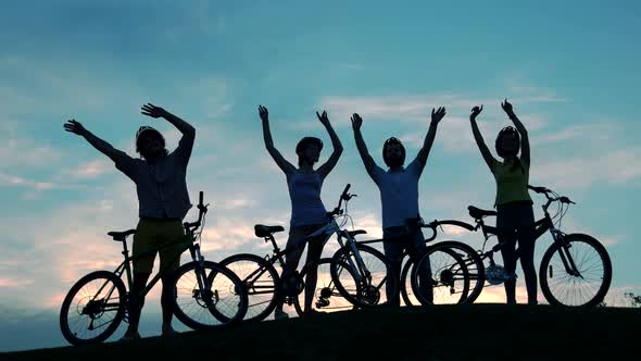 Cyclists Waving with Hands at Sunset Sky