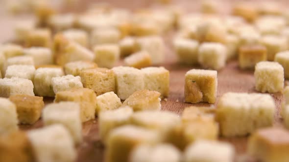 Wheat toasted fried cube croutons fall on a wooden board in slow motion