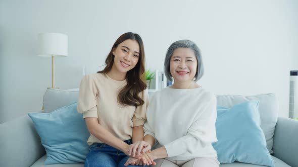 Portrait of Asian lovely family, young daughter sit with senior elder older mother on sofa in house.