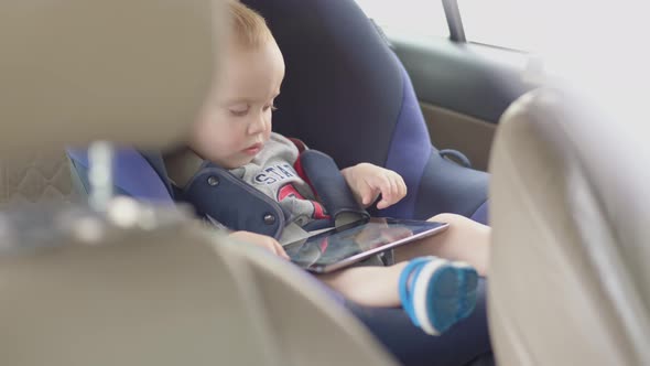 Little Child Kid Sitting in Carseat Using Digital Tablet Mobile Tapping Screen