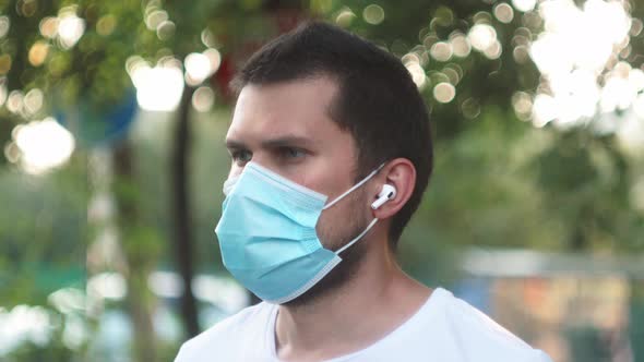 Male Man with Wireless Headphones in a Medical Protective Mask Online Listening Music During Self